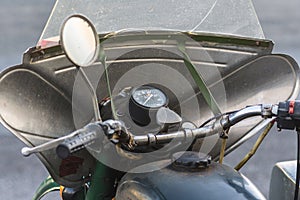 Control panel of an old and rusty green motorcycle. Old analog speedometer and switches on the headlight body. Old batwing is