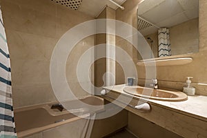 Conventional bathroom with marble countertop, brown porcelain bathtub with curtain, frameless mirror embedded in cream marble wall