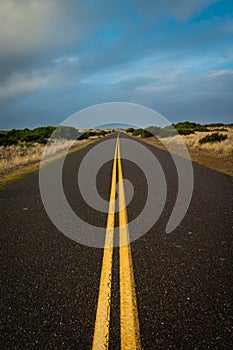 Converging lines country road with dunes and cloudy sky