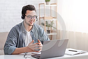 Conversation with client and video call. Guy with glasses and headset gesticulating with hands and watching laptop photo