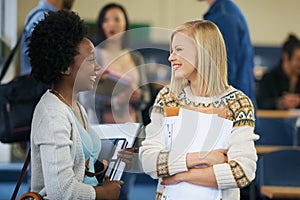 Conversation, university and women students in classroom with text books and documents for information. Smile