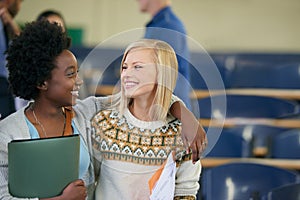 Conversation, university and women students hugging in classroom with text books for information. Smile, discussion and