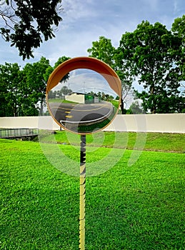 Convex safety mirror mounted on traffic pole at road curve. Asphalt road reflected in mirror. Safety device for dangerous