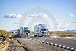 Convoy of the big rig semi trucks with different semi trailers carry cargo running on the divided highway road in both directions