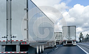 Convoy of big rig semi trucks with semi trailers running on the wide highway on several lines