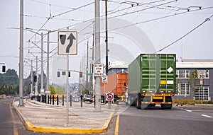 Convoy of big rig semi trucks transporting containers running on the city street with tram line