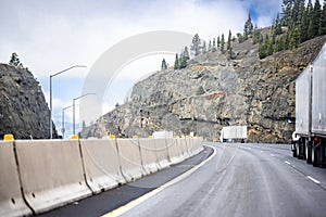 Convoy of big rigs semi trucks with semi trailers climb a mountain pass in California
