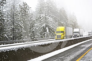 Convoy of big rigs semi trucks with semi trailers moving cautiously on a highway during a winter blizzard near Shasta Lake in