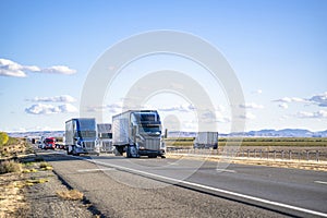 Convoy of the different big rigs semi trucks carry cargo in semi trailers running on the divided highway road in both directions