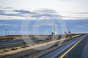 Convoy of different big rigs semi trucks with semi trailers driving on the divided straight highway road at twilight