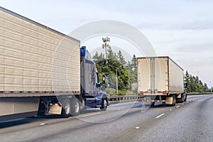 Convoy if big rig semi trucks with semi trailers transporting commercial cargo driving on the wide multiline highway road