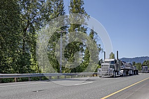 Convoy of the loaded big rigs semi trucks with cargo on flat bed semi trailers running on the multiline highway road