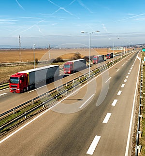 Convoy of red transportation trucks in line on a country highway