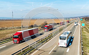 Convoy of Red transportation Trucks in line passing two white buses on a countryside highway