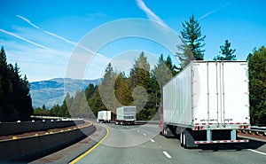 Convoy Semi trucks dry van trailers on winding highway interstate I-5 back view