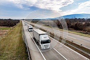 Convoy of Three White transportation trucks in line on a country highway at sunset