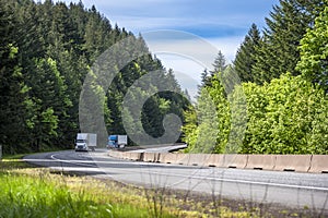 Convoy of two big rig semi trucks with reefer and dry van semi trailers running on the wide divided turning highway road with