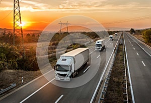 Convoy of white lorry trucks on a highway at sunset