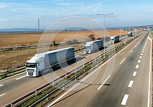 Convoy of White transportation trucks in line on a country highway