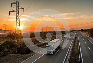 Convoy of White transportation trucks in line on a country highway at sunset