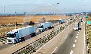 Convoy of White transportation trucks in line on a countryside highway