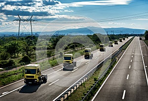 Convoy of yellow transportation semi trucks in line on a countryside highway