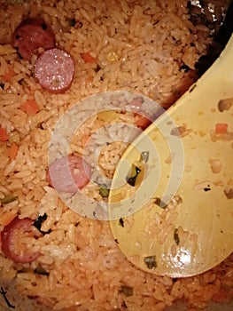 Coocked rice with a spoon inside it has sausage in it photo