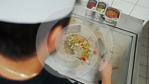 Cook adding bean sprouts, mushrooms and soy sauce to vegetable noodles on a hot plate. Overhead top down view of