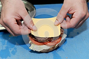 Cook adding cheese on burger. Preparing and making hamburger.