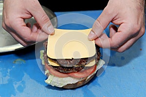 Cook adding cheese on burger. Preparing and making hamburger.