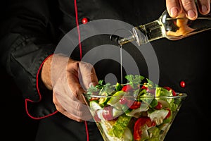 The cook adds olive oil to a vitamin salad for lunch. The concept of preparing a vegetarian dish with the hands of a chef.