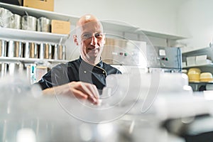 Cook in black apron smiling over detail shot of professional cooking machine in foreground and. Bald caucasian male chef