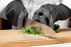 A cook in black gloves is cutting parsley