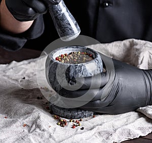 Cook in black latex gloves holding a stone mortar with pepper