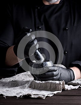 Cook in black latex gloves holding a stone mortar with pepper