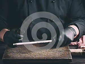 Cook in black latex gloves sharpens a knife over a wooden table