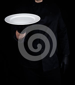 Cook in black uniform and black latex gloves holds in his hand a round empty white plate