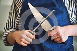 A cook in a blue apron is about to sharpen a kitchen knife on a long whetstone