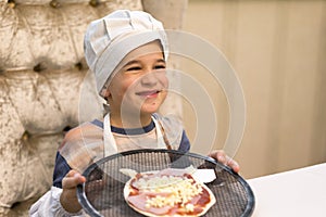 Cook boy. Little boy is a cook in flour in a white hat and apron in the kitchen preparing homemade pizza