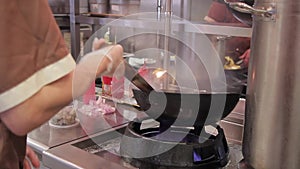 The cook of the cafe stirs vegetables in a skillet over powerful fire.