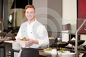 Cook or chef from catering service posing with food at buffet