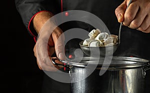 A cook cooks dumplings in a pot in a restaurant kitchen. Close-up of a chef hand holding a ladle