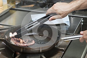 Cook cooks an octopus in a frying pan on a gas stove