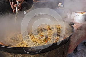 Cook cooks pilaf in a cauldron. A man interferes with rice