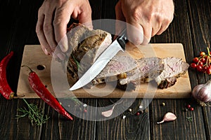 The cook cuts the baked veal meat before preparing dinner. The concept of cooking. Dark background for advertising or recipe