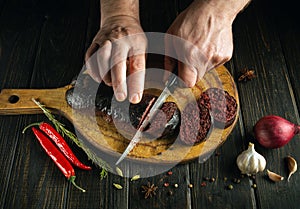 The cook cuts blood sausage with a knife on a cutting kitchen board. Cooking a national dish on the kitchen table with spices and