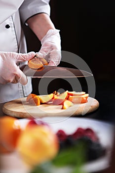 The cook cuts the fruit into slices. Assorted fruits and berries are cut into pieces. Unrecognizable vertical photo. Only hands