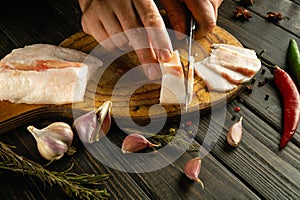 The cook cuts lard with a knife on a wooden cutting board to prepare sandwiches with garlic. Delicious peasant food concept