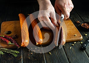 The cook cuts the meat sausage with a knife before frying. Cooking sausages on the kitchen table by the hands of a chef