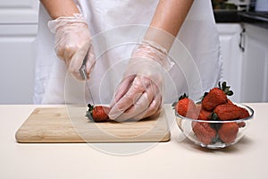 the cook cuts off the tails of strawberries on a wooden board close-up of hands